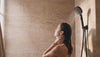 Femme sous la douche à l'italienne en travertin avec le pommeau de douche noir mat Maison Bréa